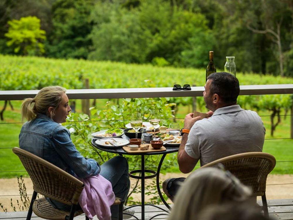 A couple enjoying selection of food and wine on the decking of a vineyard. 