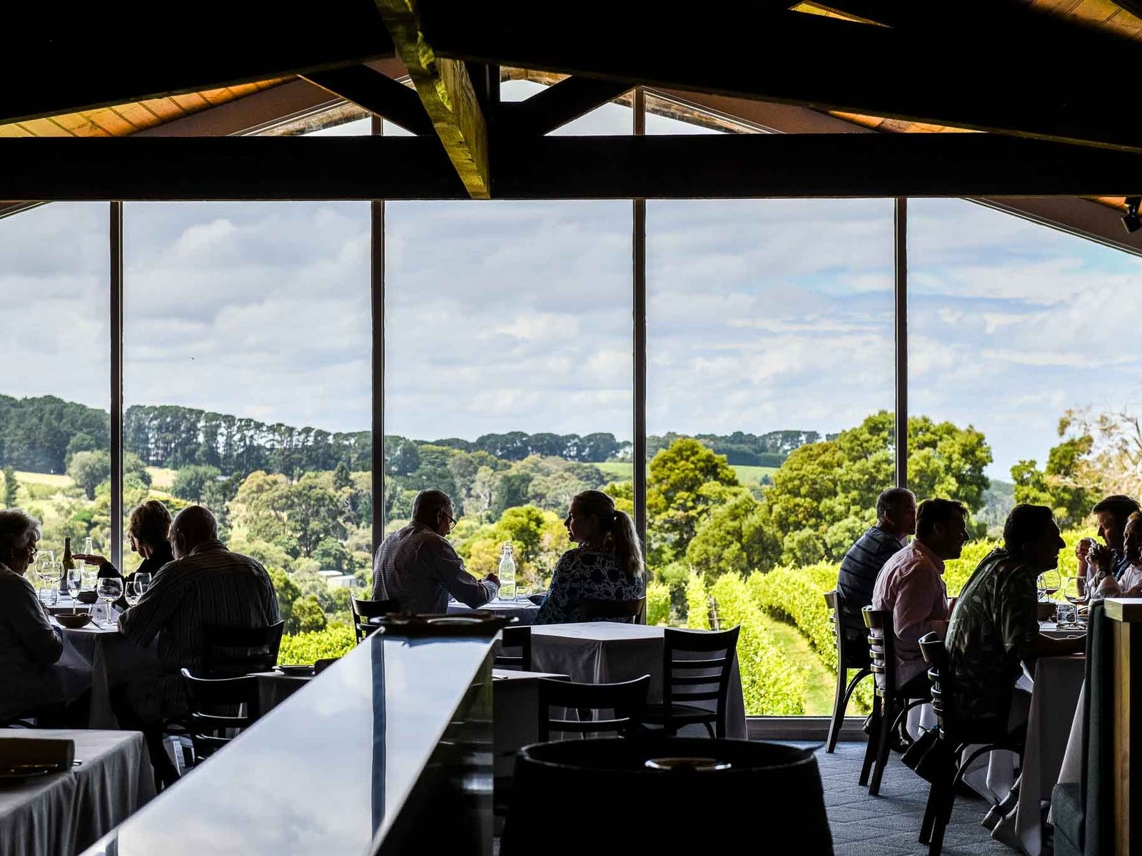 People sitting on tables at Paringa Estate in front of floor to ceiling windows, overlooking vineyards.